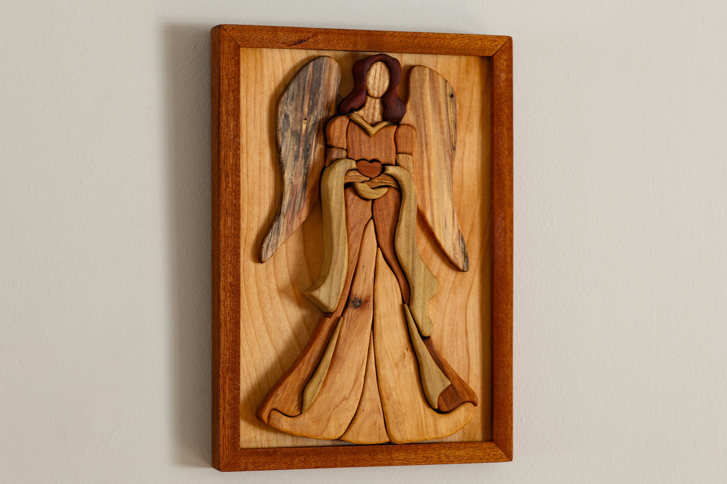 Wooden angel frame is made from 9 different species of wood. Each piece is hand-cut and puzzled together to form an angel. Angel is attached to a wooden frame.
