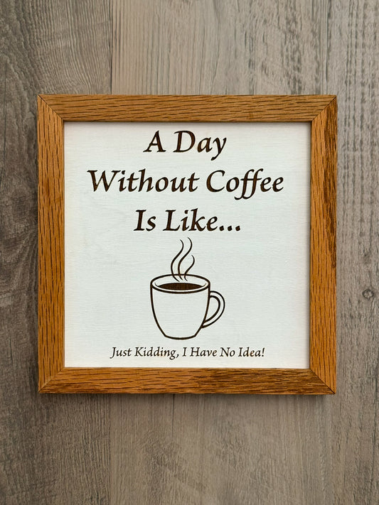 White-painted square wooden sign, framed with oak wood, features a laser-engraved message, "A Day Without Coffee Is Like... Just Kidding, I Have No Idea," alongside a steamy cup of coffee design.