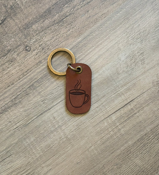 Brown rounded rectangle leather keychain with a brass key ring and jump ring. With a coffee cup laser-engraved on it. Approx. 1" X 2". 