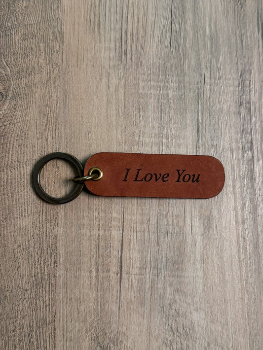 Brown rounded rectangle leather keychain with a brass key ring and jump ring. With the words "I Love You" laser-engraved on it. Approx. 1" X 3". 